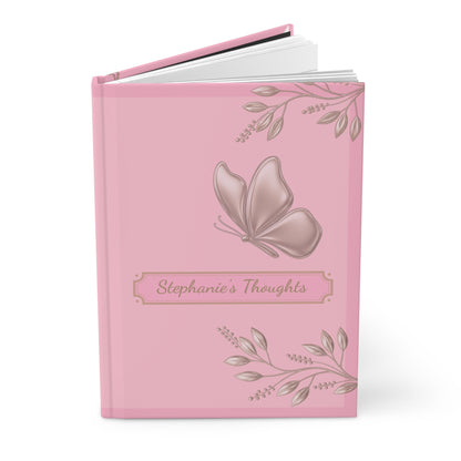 A pink hardcover journal with a butterfly and floral illustration on the cover, featuring the text 'Stephanie's Thoughts' on a white background.