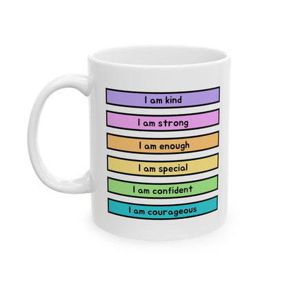 A white ceramic mug with a colorful printed graphic showing six horizontal colored bars in purple, pink, orange, yellow, green, and blue, each with text starting with 'I am' such as 'I am kind', 'I am strong', 'I am enough', 'I am special', 'I am confident', and 'I am courageous'.
