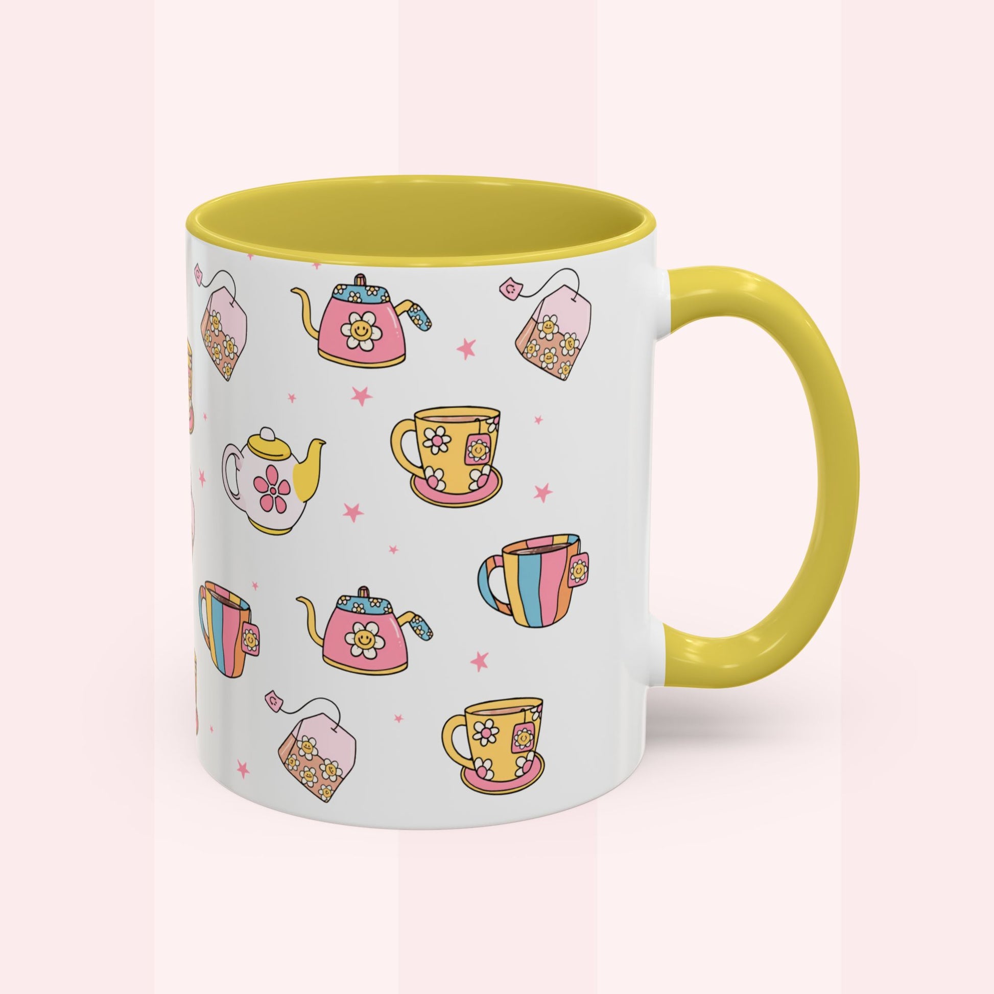 A white ceramic mug with a yellow interior and handle, decorated with a colorful pattern of teapots, teacups, and tea bags on a soft pink background.