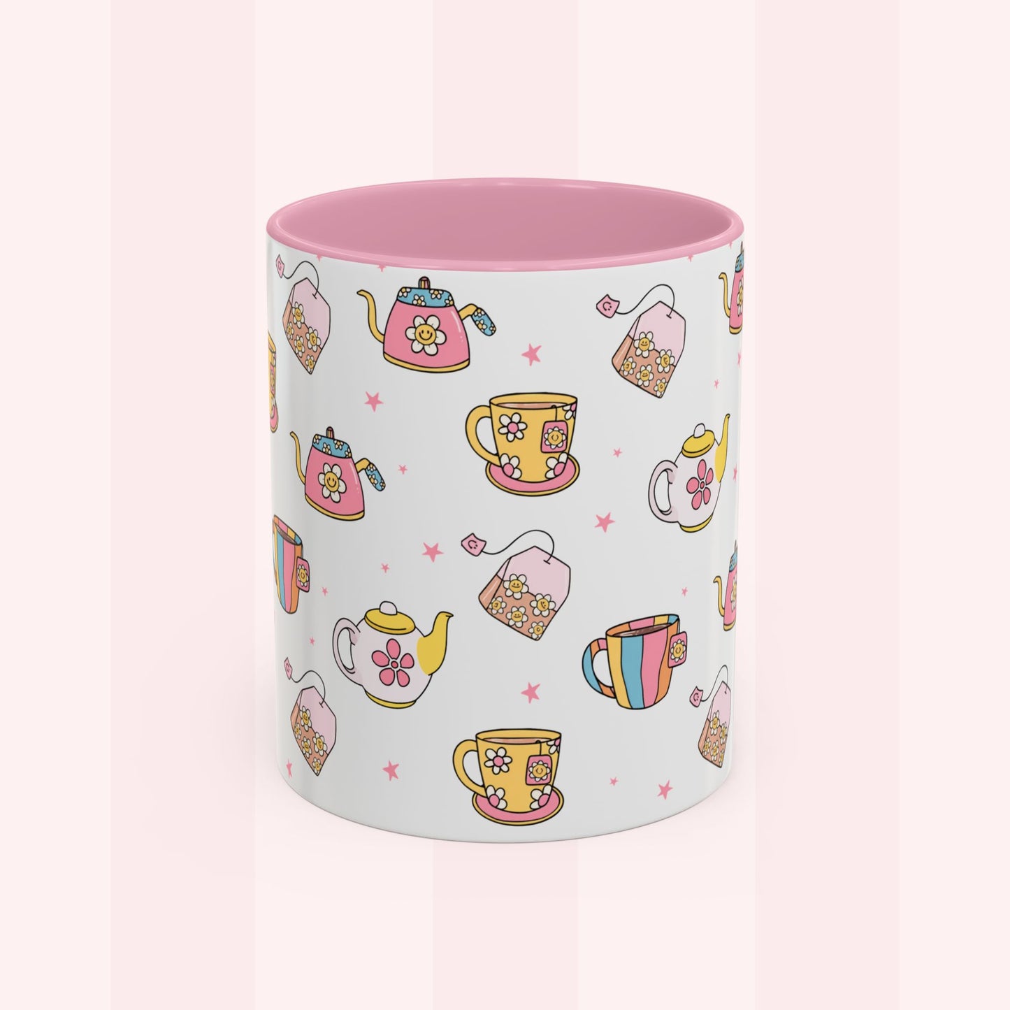 A white ceramic mug with a pink interior, decorated with a repeating pattern of colorful teapots, teacups, teabags, and small pink stars on a pale pink striped background.
