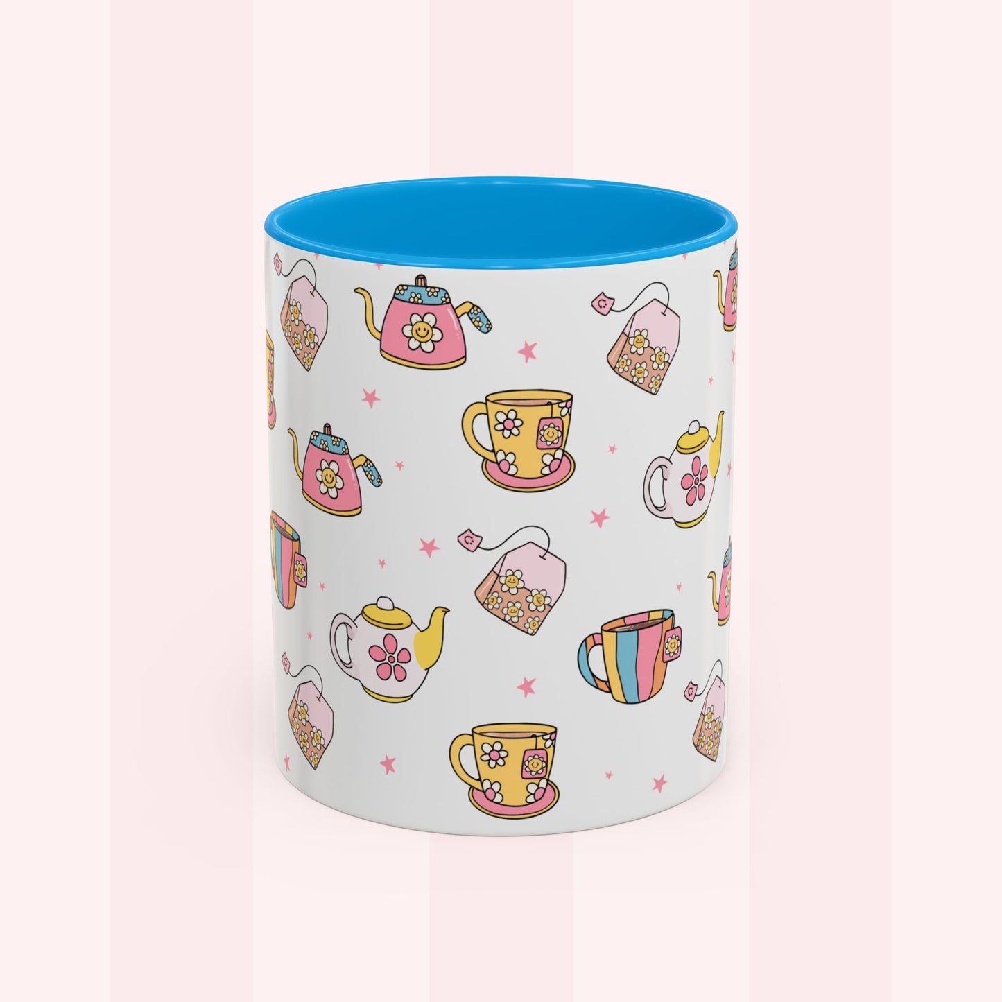 A white ceramic mug with a bright blue interior, decorated with a repeating pattern of colorful teapots, teacups, and tea bags on a soft pink striped background.