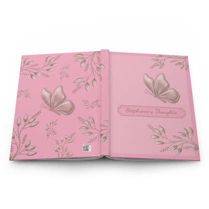 An open pink keepsake album or journal with butterfly and floral illustrations, featuring the title 'Stephanie's Thoughts' on the right page.