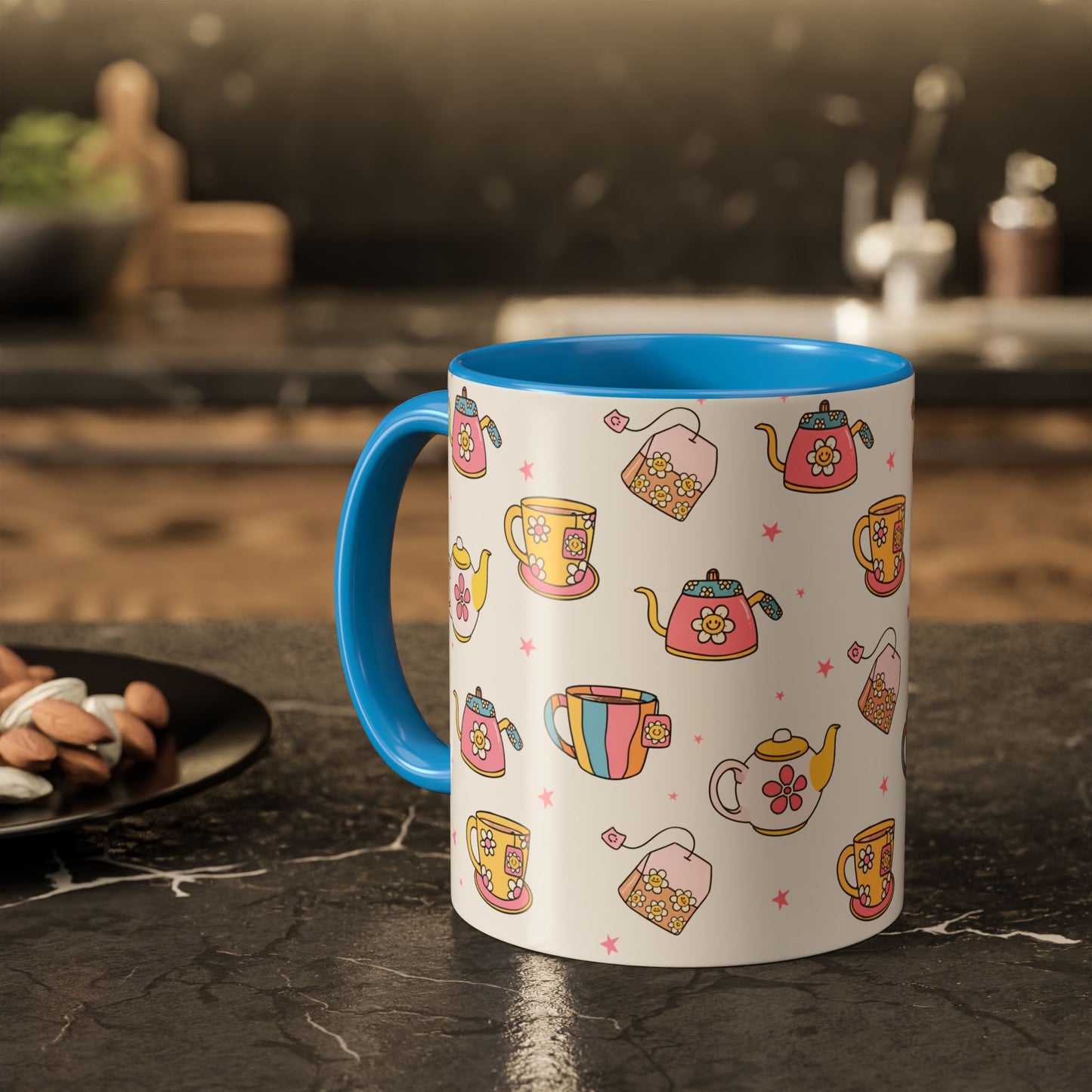 A white ceramic mug with a bright blue handle and interior, decorated with a colorful pattern of teapots, teacups, and tea bags on a dark kitchen countertop.