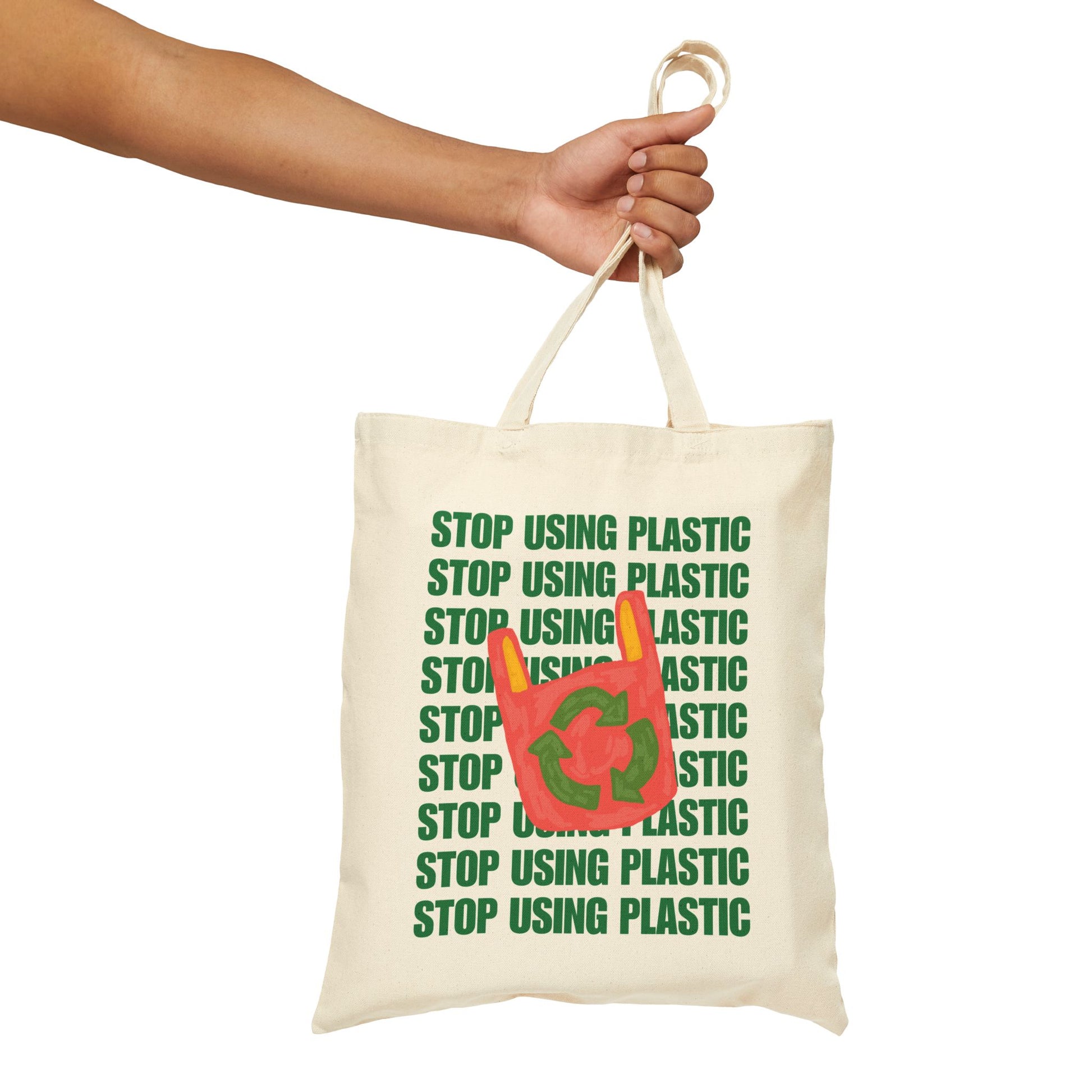 An off-white canvas tote bag with green text reading 'STOP USING PLASTIC' and a red plastic bag graphic with a recycling symbol, held by a person's hand against a white background.