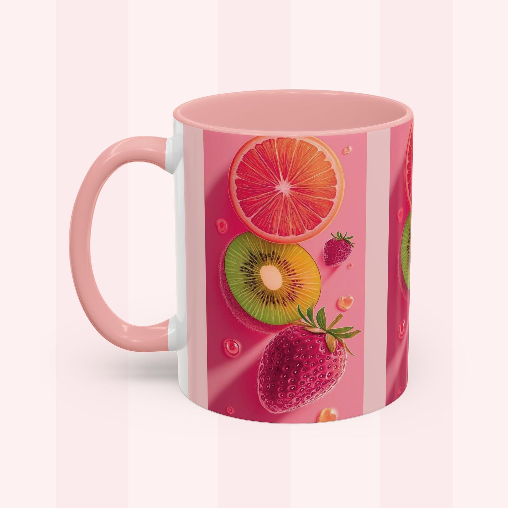 A pink ceramic mug featuring a vibrant fruit print with sliced orange, kiwi, strawberries, and grapefruit on a pink striped background, set against a pale pink striped backdrop.