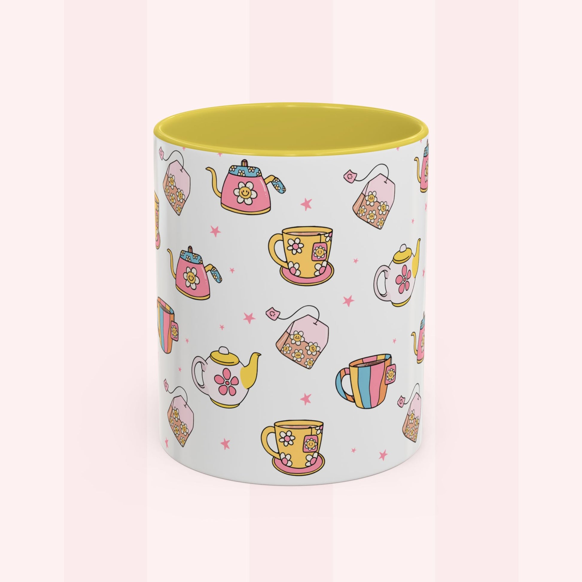 A white ceramic mug with a yellow interior, decorated with a repeating pattern of colorful teapots, teacups, teabags, and small pink stars on a pale pink striped background.