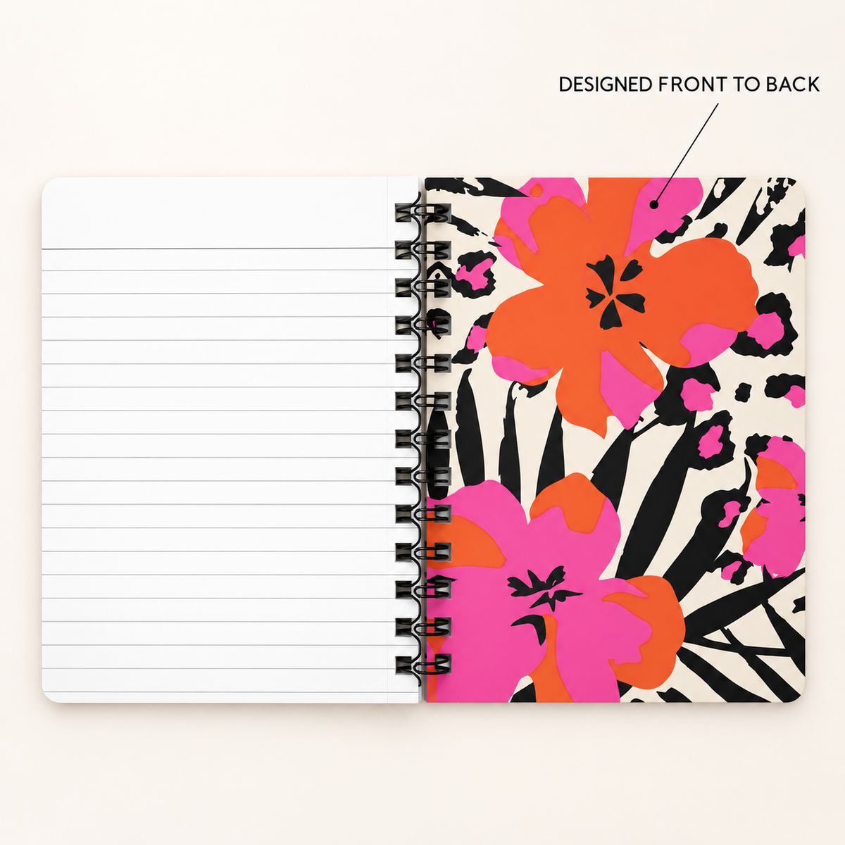 A spiral-bound notebook shown open on a light beige background, with lined blank pages on the left and a bold floral cover design on the right. The cover features large orange, pink, and black flowers on a white base, with text above reading 'DESIGNED FRONT TO BACK'.