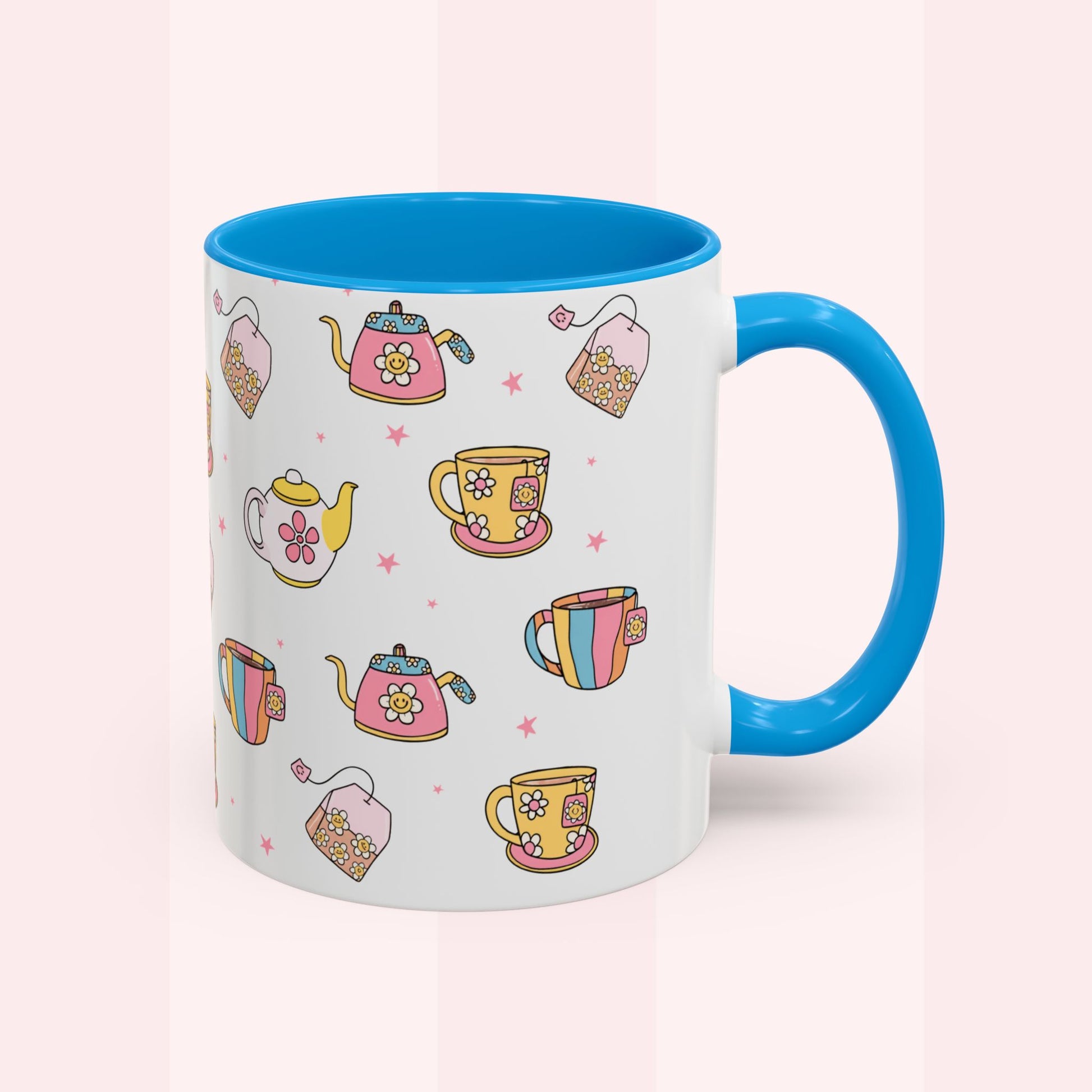 A ceramic mug with a white exterior decorated with colorful illustrations of teapots, cups, and tea bags, featuring a bright blue interior, handle, and rim, set against a pale pink background.