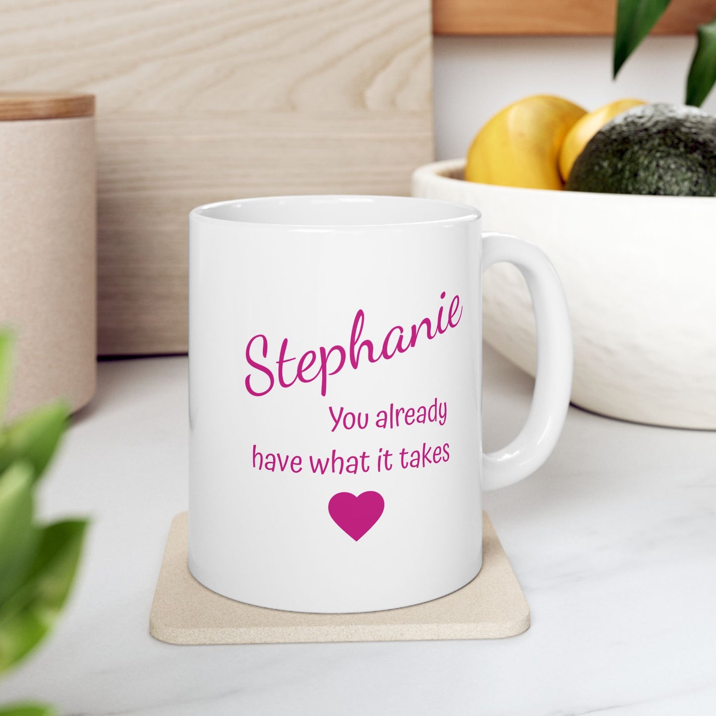 White mug with pink text and a heart on a white surface with plants and a plant pot in the background