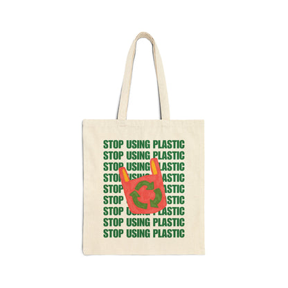An off-white canvas tote bag with green text reading 'STOP USING PLASTIC' repeated vertically, overlaid with a red plastic bag graphic containing the green recycling symbol.