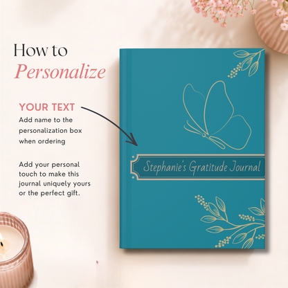 A teal personalized hardcover journal with gold butterfly and floral line art, shown on a light cream background with decorative props. Text on the left explains how to personalize the journal with a name and suggests adding personal touches.