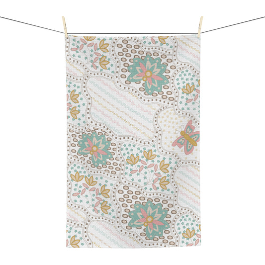 A rectangular fabric tea towel with a vintage bohemian floral pattern, hanging from a clothesline with wooden clips against a solid white background.