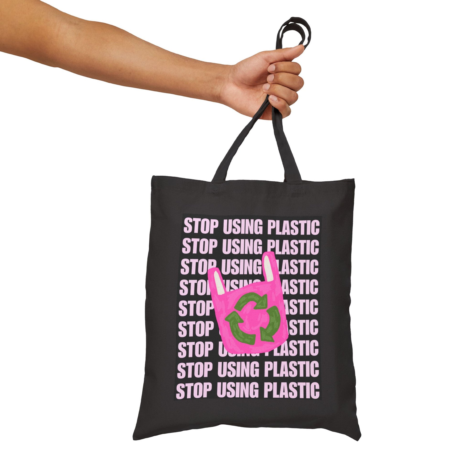 A black canvas tote bag with a pink recycling symbol and the text 'STOP USING PLASTIC' repeated in pink, held by a person's arm against a white background.