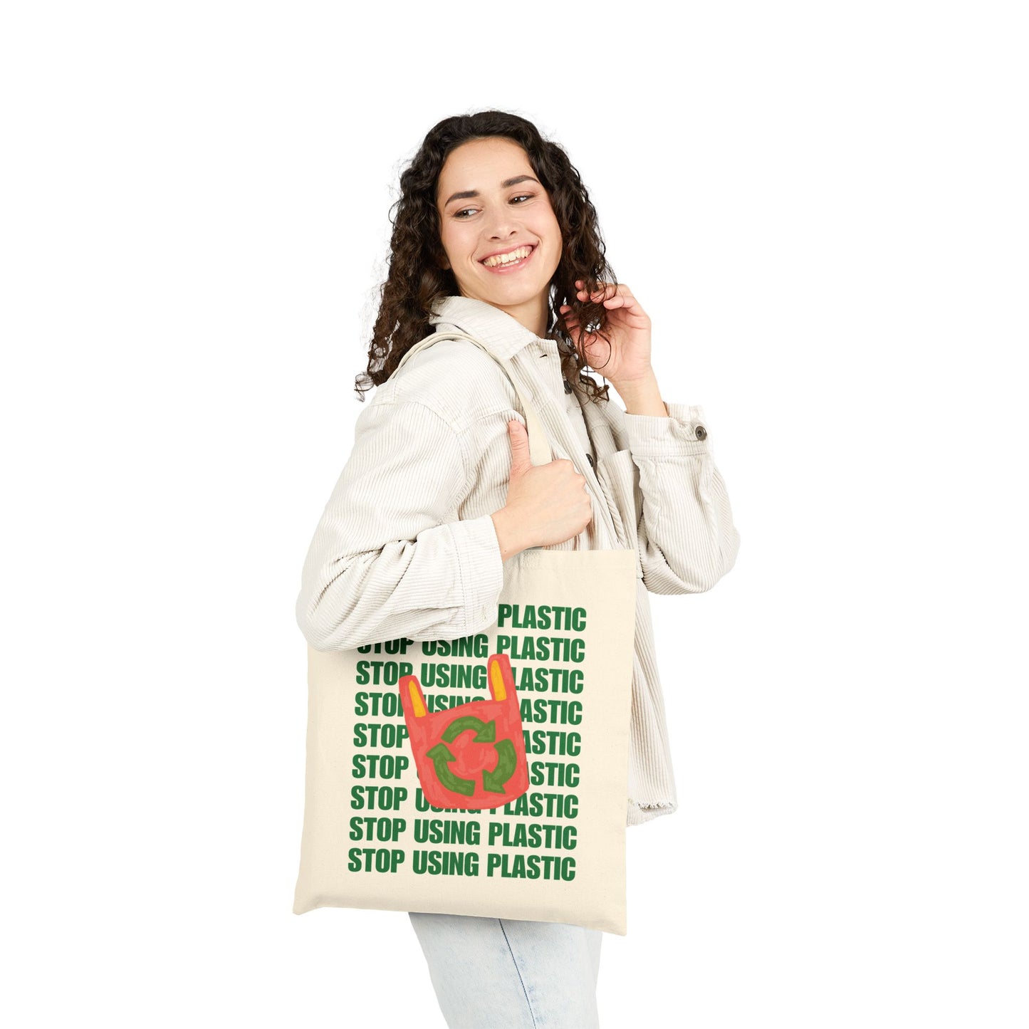 A woman wearing a light beige hooded sweatshirt and light blue jeans holds a cream-colored canvas tote bag. The bag features a green graphic with the text 'STOP USING PLASTIC' repeated vertically, overlaid with a red circular icon showing a plastic bottle and a green leaf.