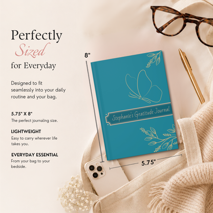 A teal gratitude journal with white floral line art and the text 'Stephanie's Gratitude Journal' shown in a styled flat lay. The image includes measurement callouts indicating 8 x 5.