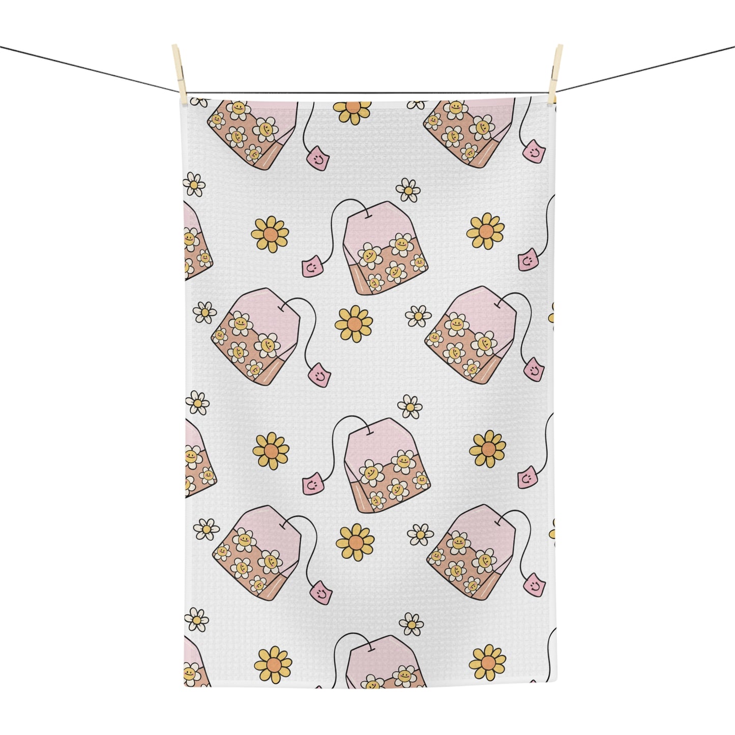 A white kitchen tea towel with a repeating pattern of pink teabags filled with yellow and white flowers, hanging from a string with wooden clips against a white background.