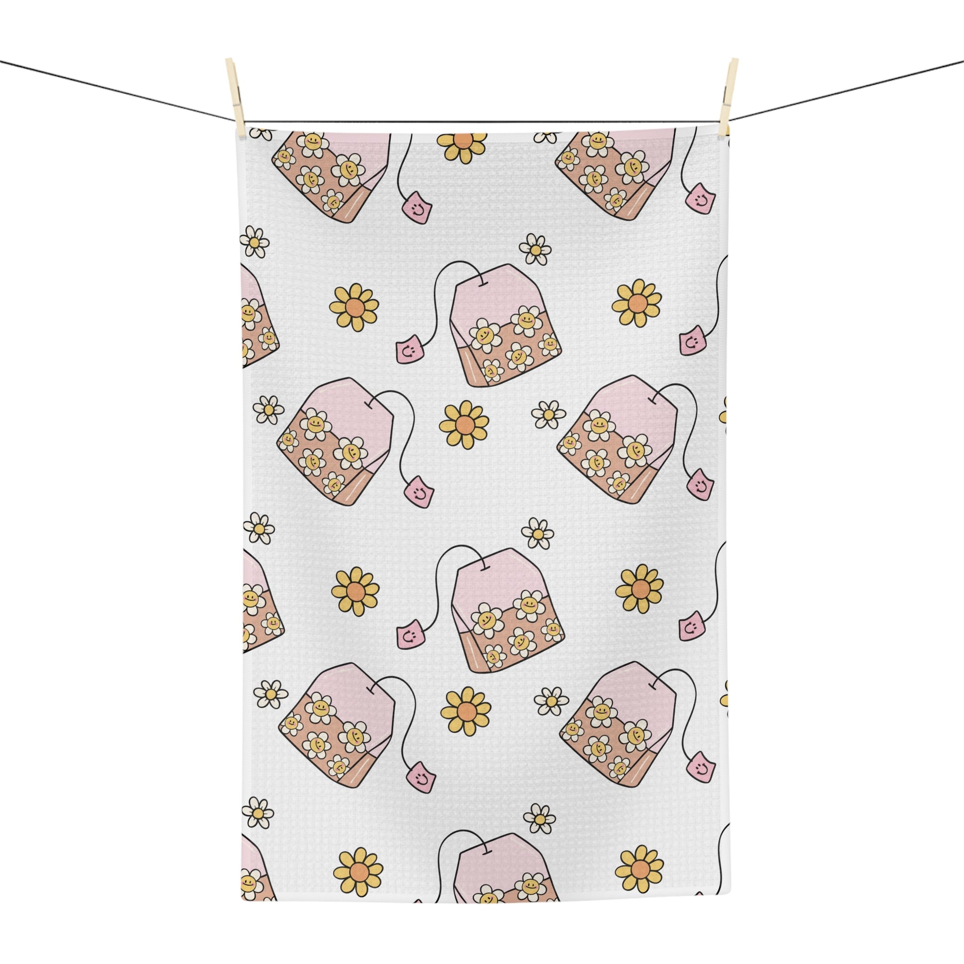 A white kitchen tea towel with a repeating pattern of pink teabags filled with yellow and white flowers, hanging from a string with wooden clips against a white background.
