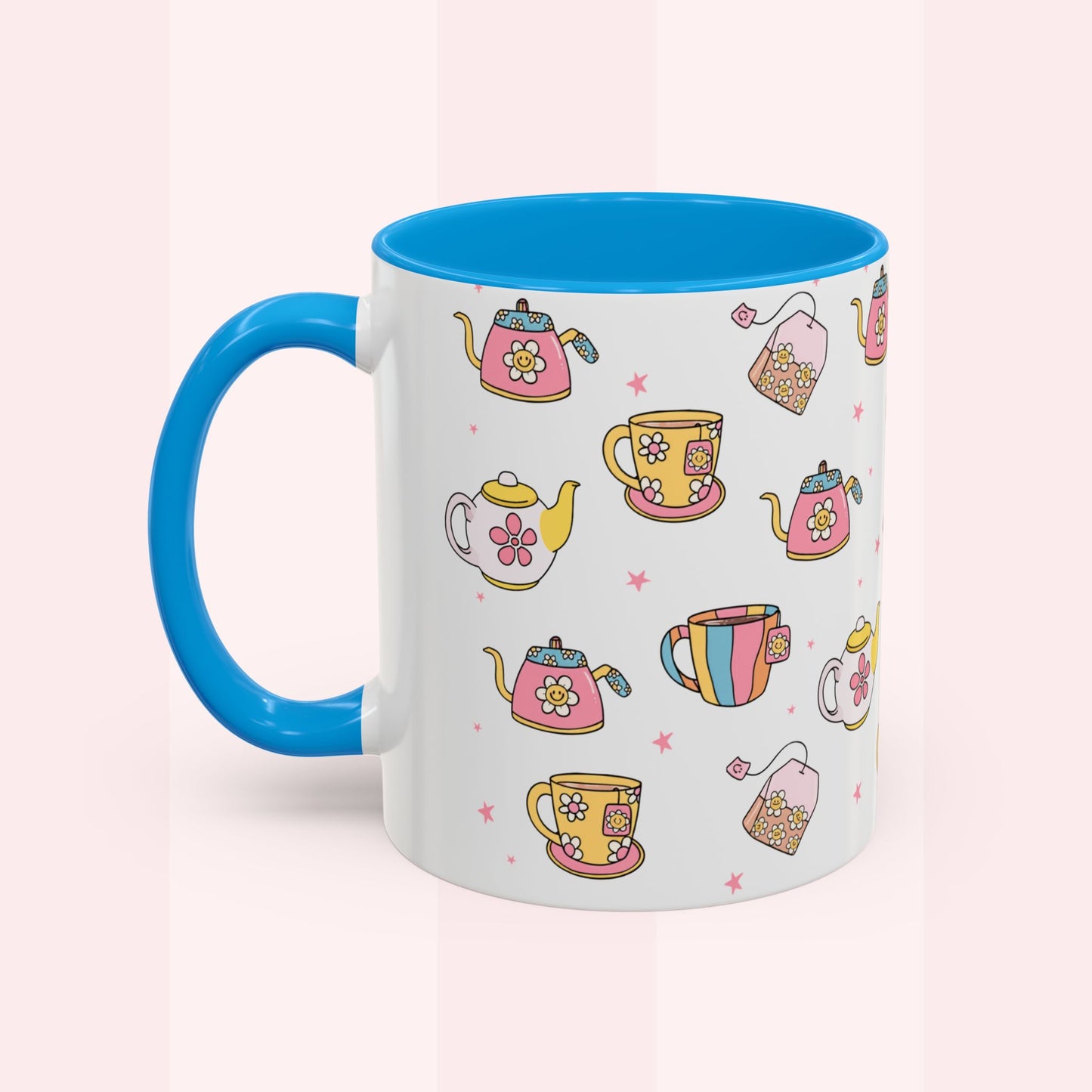 A white ceramic mug with a bright blue handle and interior, decorated with a colorful pattern of teapots, teacups, and tea bags on a soft pink background.