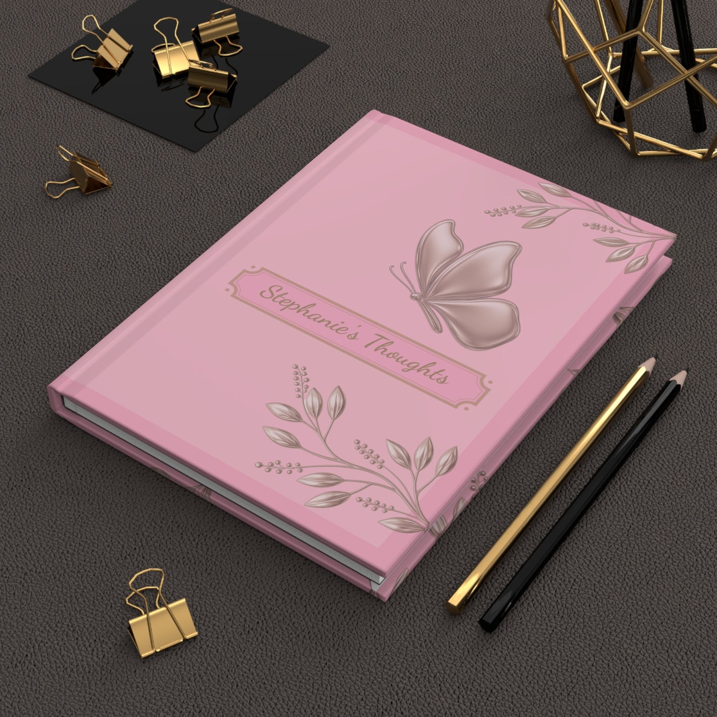Notebook with blue floral design on a black and white striped background, surrounded by office supplies on a dark surface.