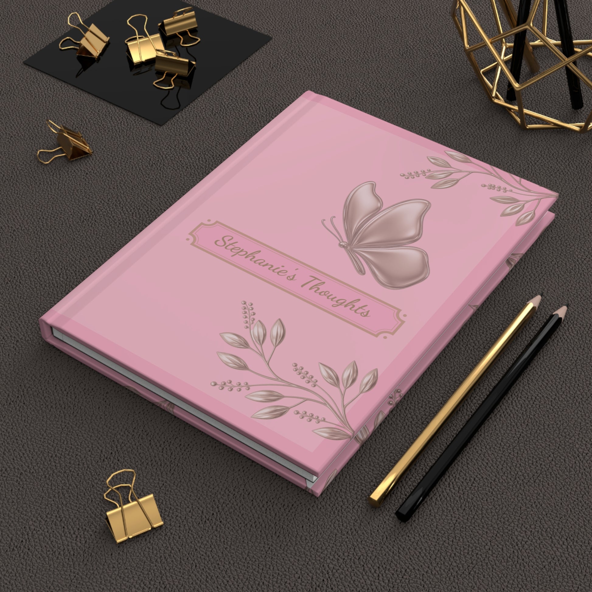 Notebook with blue floral design on a black and white striped background, surrounded by office supplies on a dark surface.