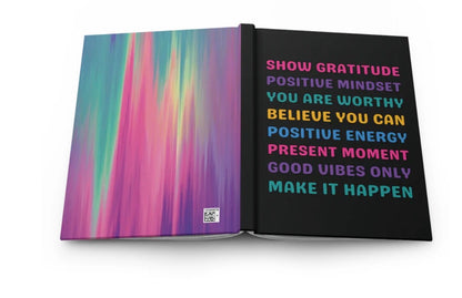 An open notebook or journal on a white background, showing a colorful abstract gradient cover on the left page and a black right page with motivational text in pink, purple, yellow, and blue.